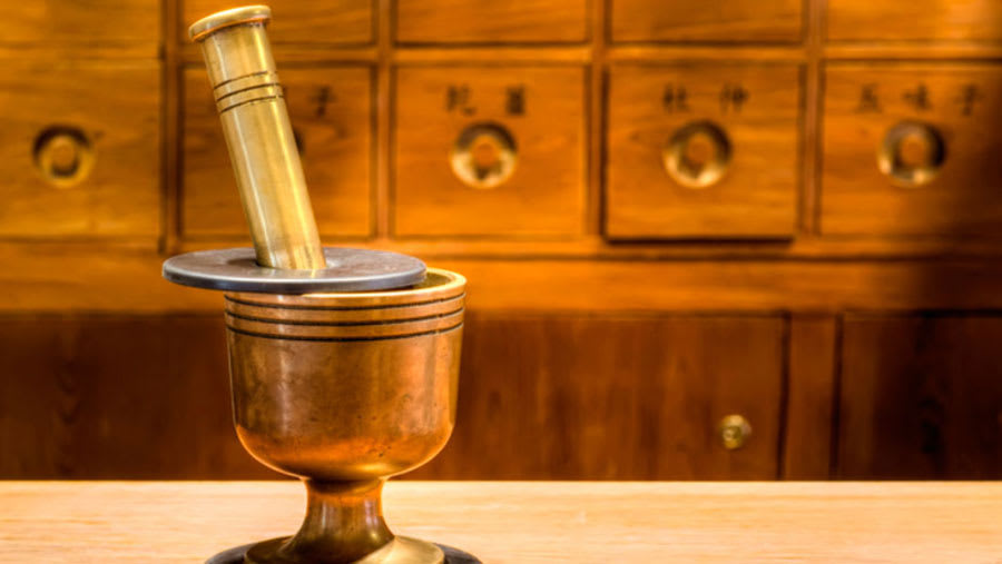 Copper mortar and pestle in front of wooden drawer shelves in background
