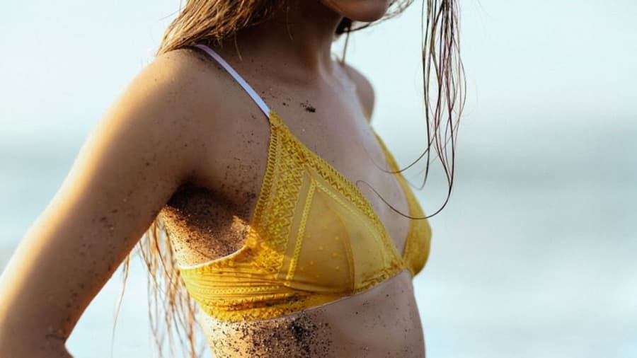 Girl with wet hair on beach in yellow bikini with dirt on side of abdomen