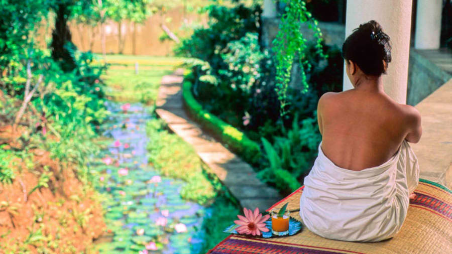 woman in Sri Lanka sitting outside near pillar next to gentle stream filled with lotuses