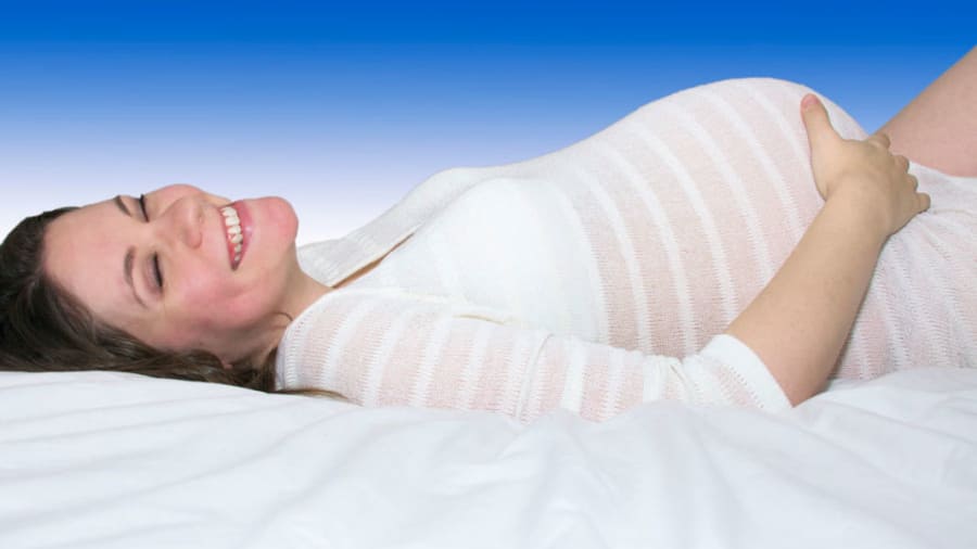 Pregnant woman lying on bed in a striped shirt with a blue wall behind her