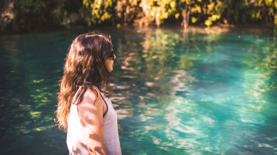 Brunette woman with sunglasses standing in sunshine next to blue pond