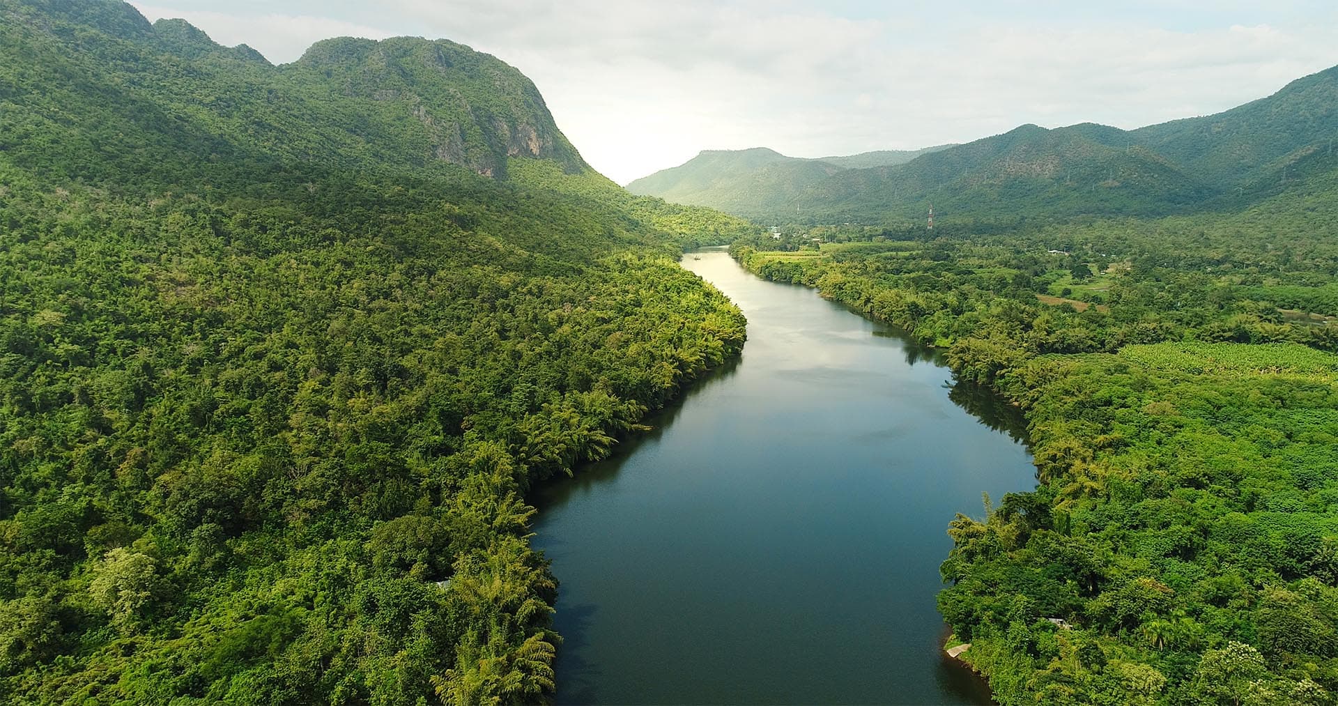 Weite Flusslandschaft als Symbol für Ruhe und Klarheit. Ein breiter Fluss schlängelt sich durch ein Tal mit dichten, grünen Wäldern und sanften Bergen am Horizont. Die unberührte Natur lädt zum Innehalten ein.