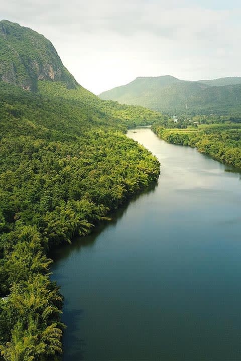 Weite Flusslandschaft als Symbol für Ruhe und Klarheit. Ein breiter Fluss schlängelt sich durch ein Tal mit dichten, grünen Wäldern und sanften Bergen am Horizont. Die unberührte Natur lädt zum Innehalten ein.