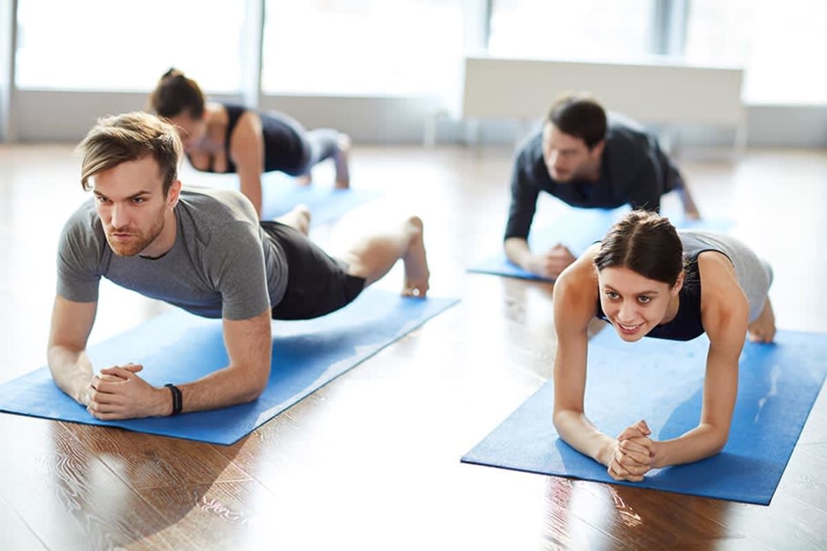 Vier Erwachsene halten in einem hellen Fitnessraum die Plank-Position.