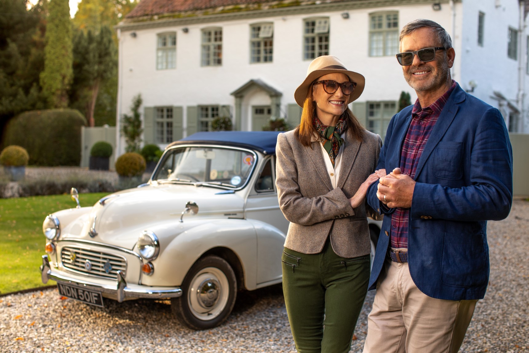 A happy couple with sunglasses in front of a car.