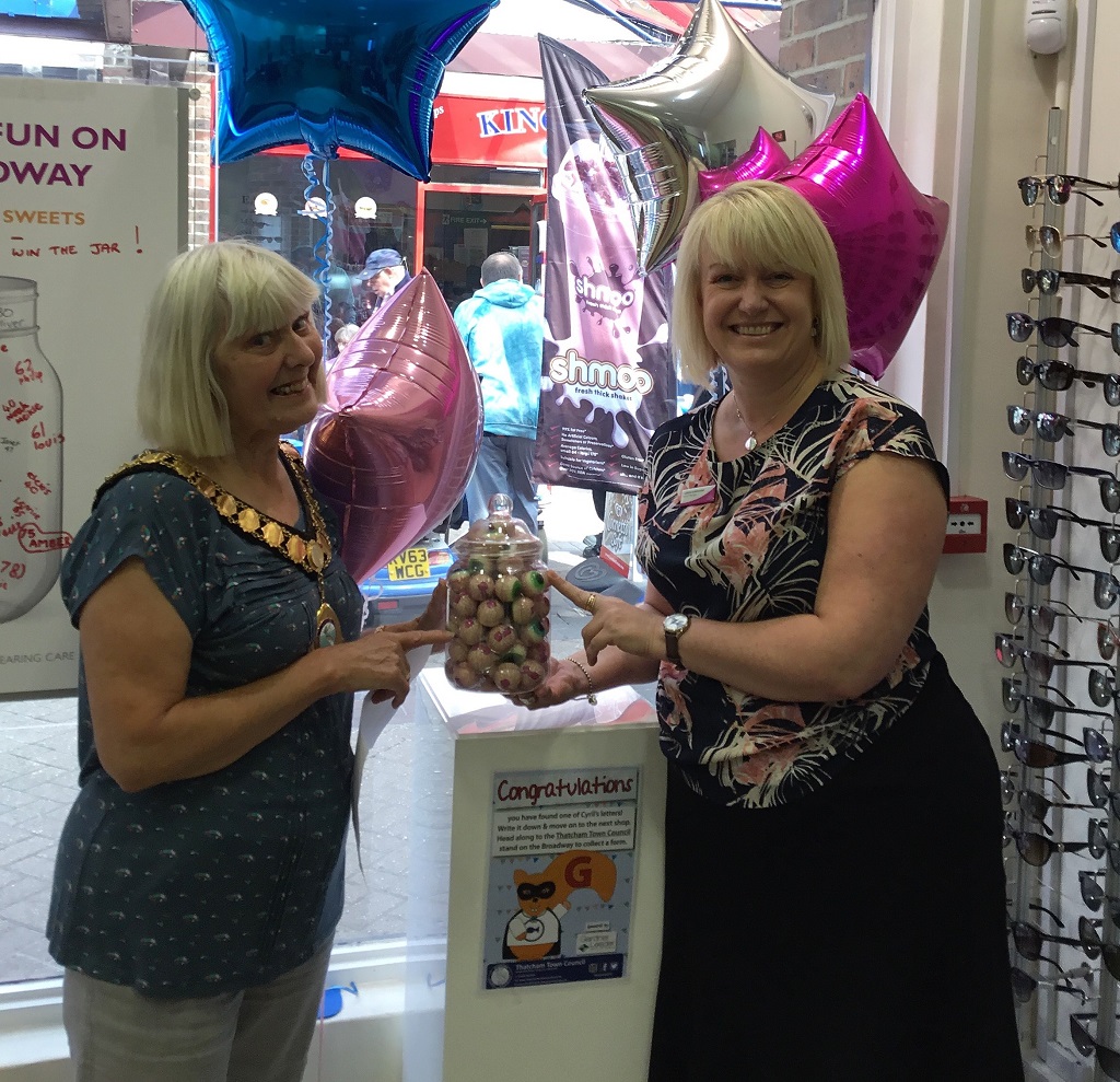 Two ladies smiling and carrying a jar full of sweets shaped like eyeballs.