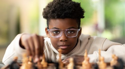 A boy wearing glasses and playing chess.