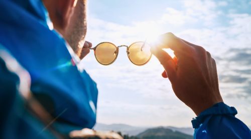 Backpacker man looking at bright sun through polarized sunglasses enjoying mountain landscape.