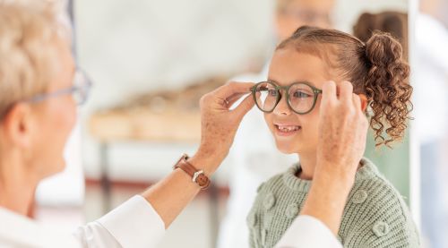 Eye doctor fitting green glasses on a young child.
