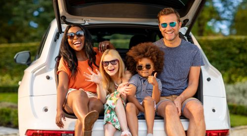 A family of four wearing sunglasses, sitting in the boot of a car, enjoying a sunny day together.