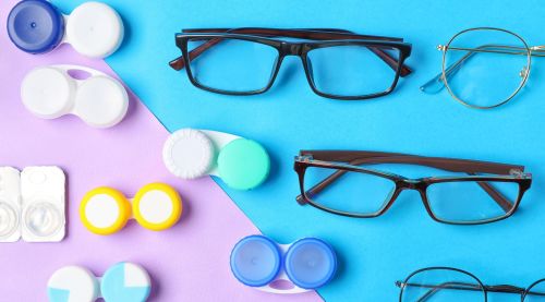 Containers holding contact lenses alongside eyeglasses, displayed against a colorful background.
