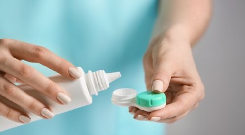 Close-up of a woman pouring contact lens solution into a container holding contact lenses.