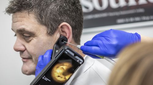 Healthcare professional performing manual ear wax removal on a patient using specialised tools.