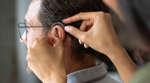 Close up side view of audiologist fitting hearing aid to man.
