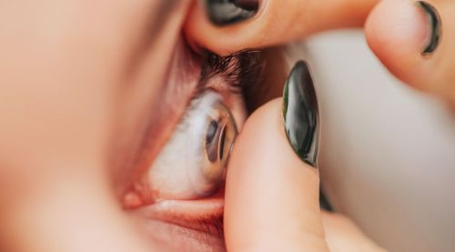 A close-up of a woman carefully inserting a contact lens into her eye.