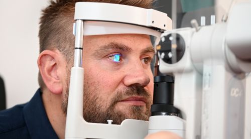 A patient undergoing an eye examination, seated at a slit lamp biomicroscope.