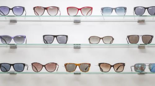 Three wall shelves displaying a variety of sunglasses, showcasing different styles, colors, and designs in an organised arrangement.