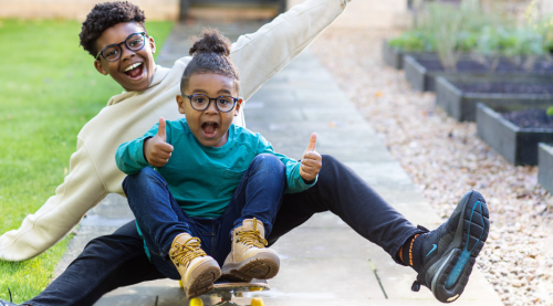 Two children playing outside on a skateboard.