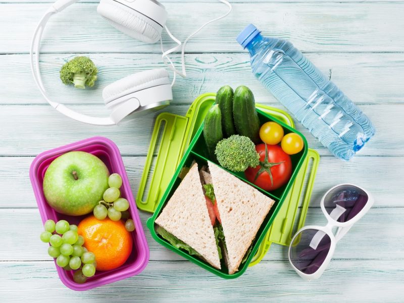 Person's lunch box next to headphones and sunglasses