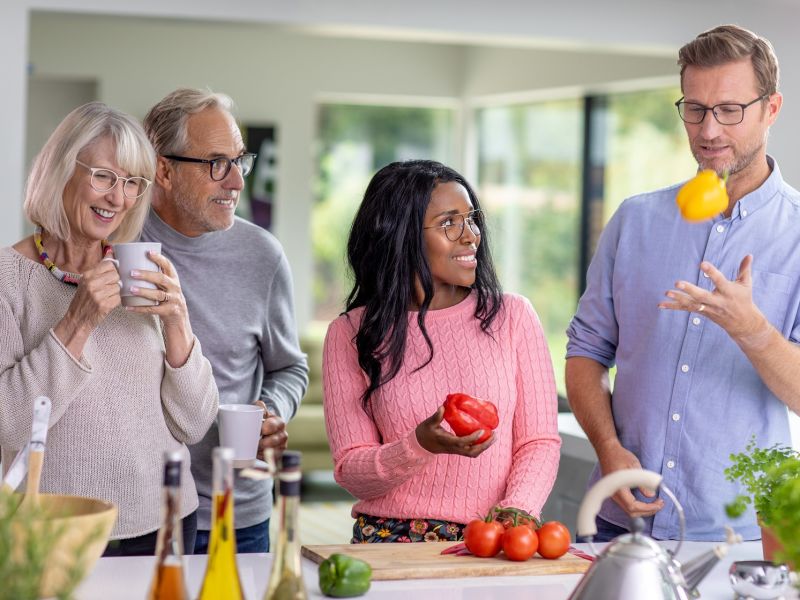 Two couples in a kitchen preparing food and laughing