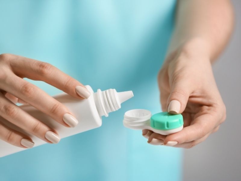 Close-up of a woman pouring contact lens solution into a container holding contact lenses.