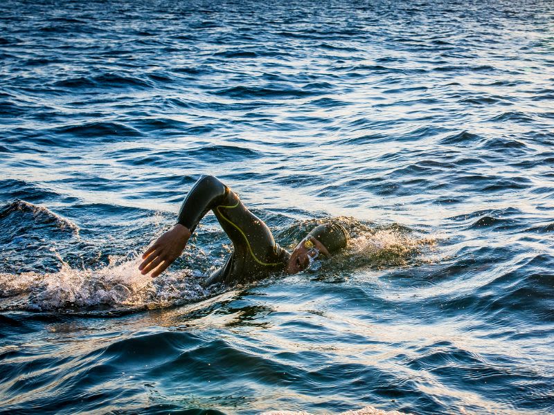 A man wearing swimsuits, sunglasses, and a hat swimming in the sea.