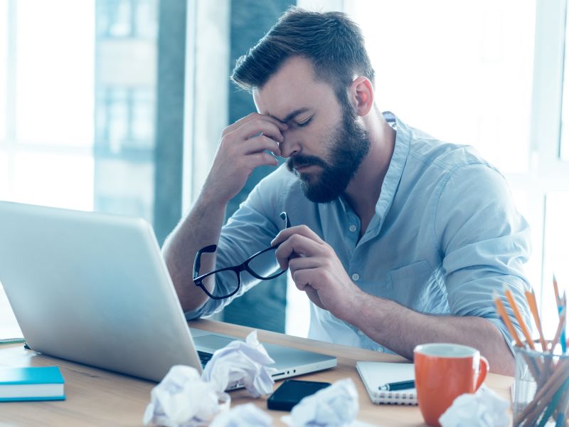 Man on laptop stressed holding nose and glasses