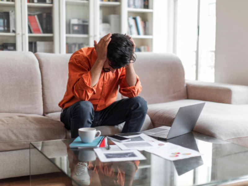 A man sitting on a sofa appears to be experiencing a migraine.