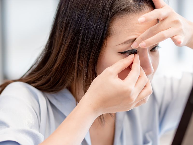 woman trying to put contact lenses into her eyes and looking to the mirror.
