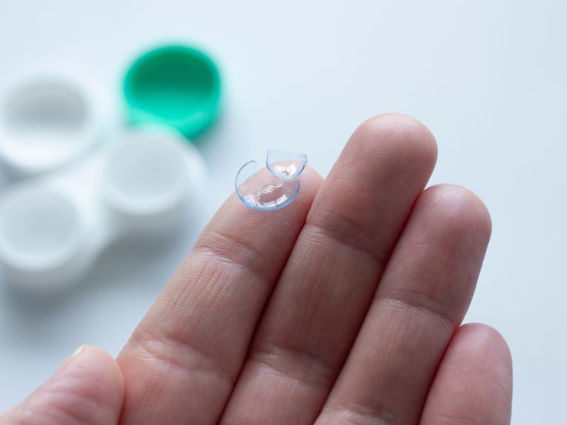 Close-up of a hand holding a damaged contact lens split into two pieces.