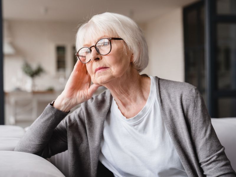 An elderly woman sitting on a sofa, lost in thought.