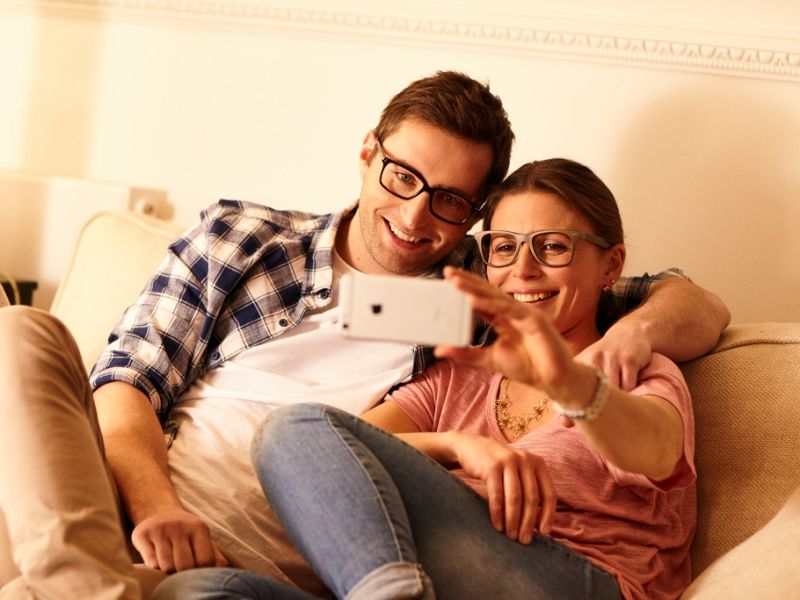 Couple on sofa wearing glasses and taking a selfie