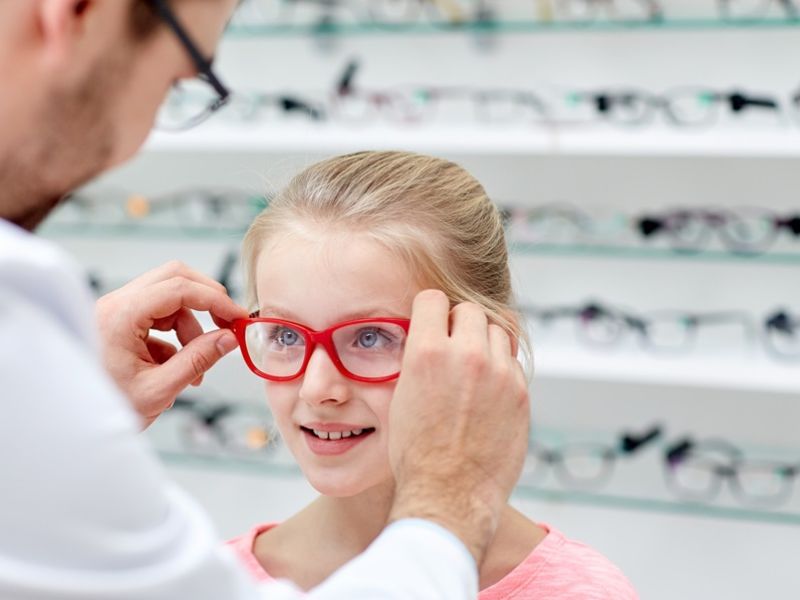 A dispensing optician fitting glasses on a young girl.