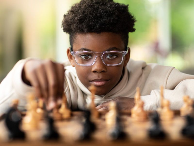 A child wearing glasses while playing chess.