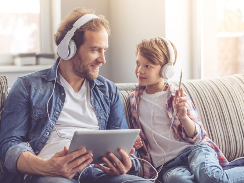 man and son on sofa listening to headphones