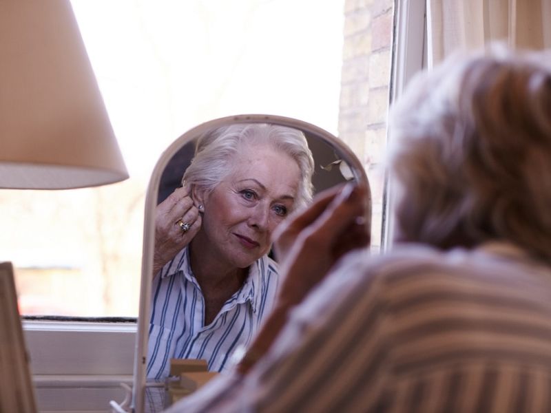 Woman inserting hearing aid looking in mirror