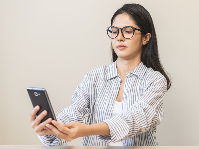 Middle-aged woman wearing eyeglasses, holding her smartphone at a distance to read a text message.