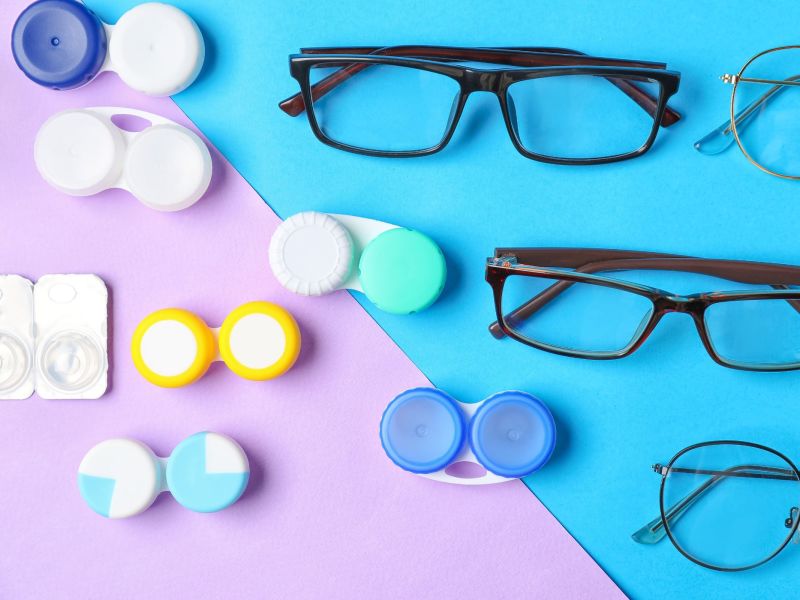 Containers holding contact lenses alongside eyeglasses, displayed against a colorful background.