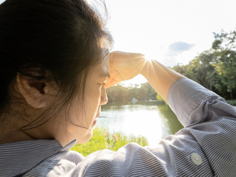 A woman experiencing light sensitivity and covering face by hand of bright sun in outdoor on sunny day.