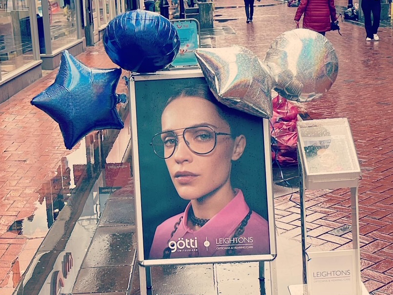 Leightons sign promoting Götti eyewear brand on a street with a star balloons.