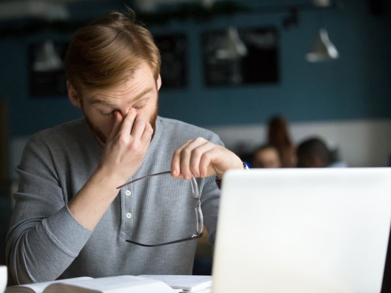 Man on laptop stressed holding nose and glasses