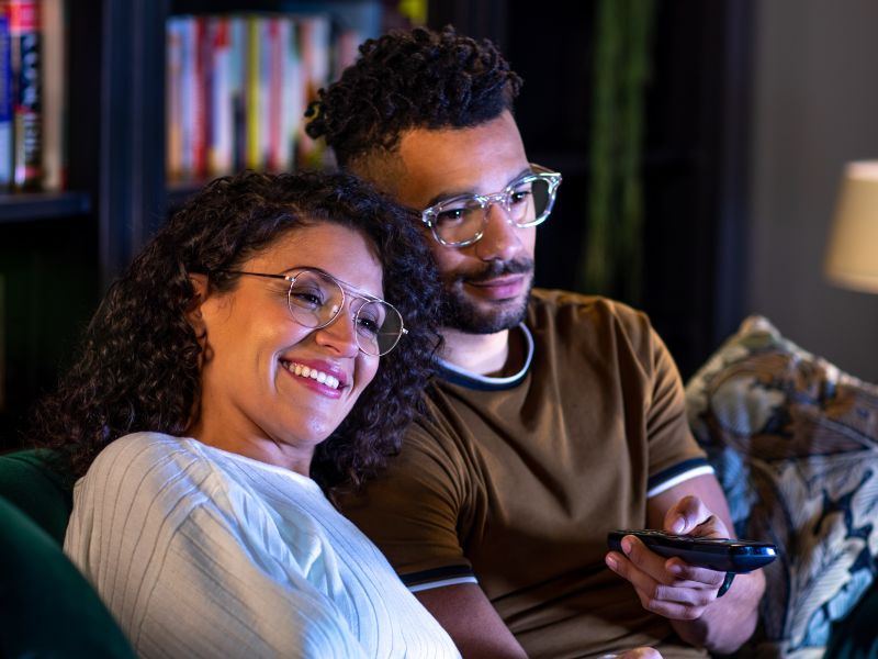 A couple sitting in a sofa and watching TV.