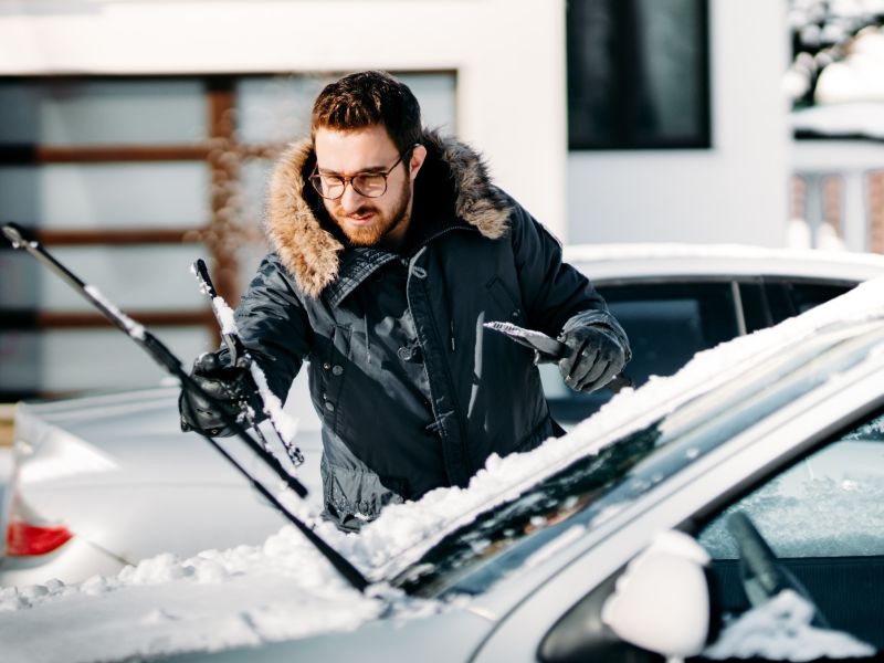 Young man in glasses preparing his car for the snow