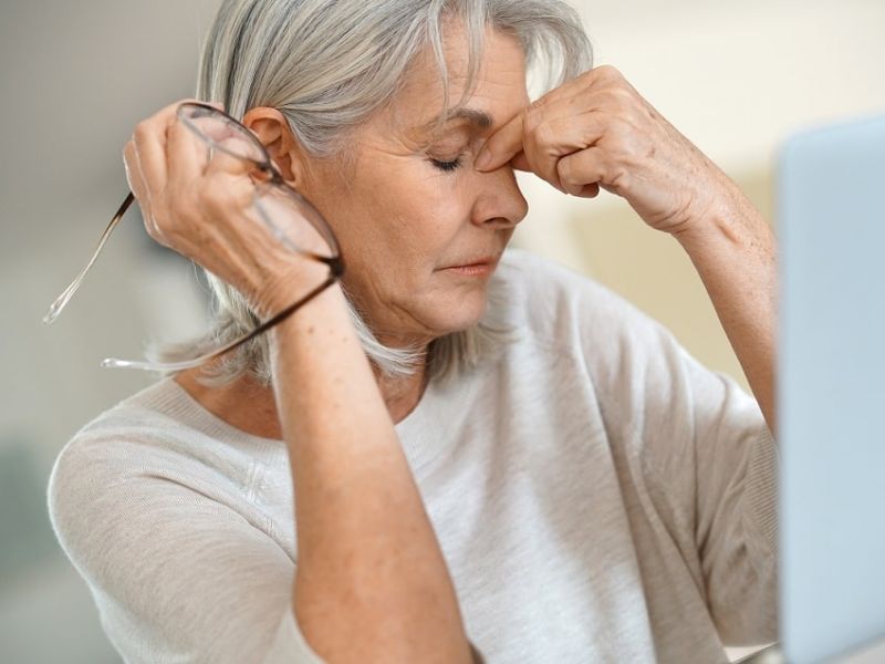 Woman having a migraine, holding glasses and nose