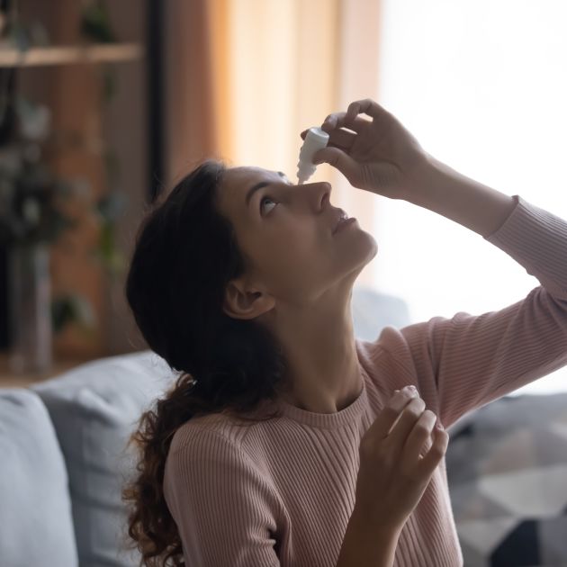 A woman putting eye drops in her eyes.