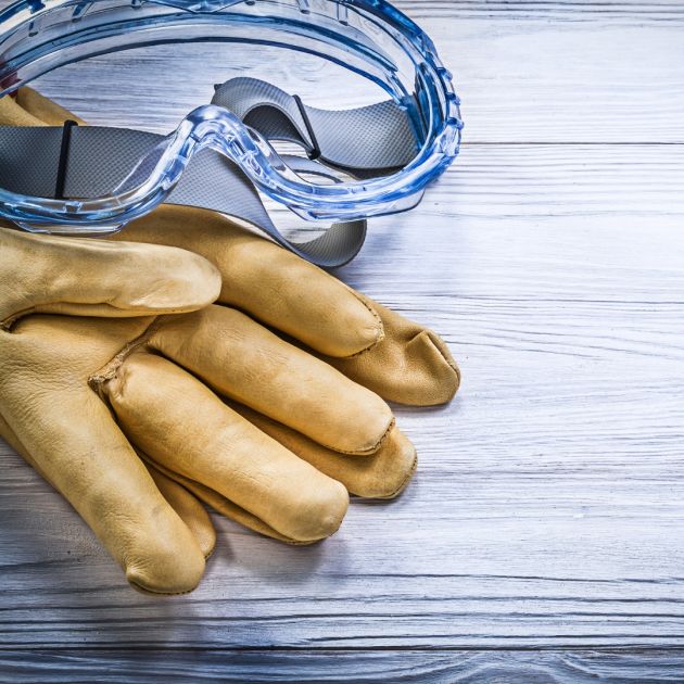 Safety goggles and gloves on a wooden surface.