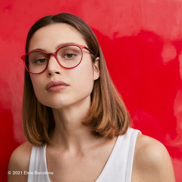 A woman wearing Etnia Barcelona red glasses on a red background.