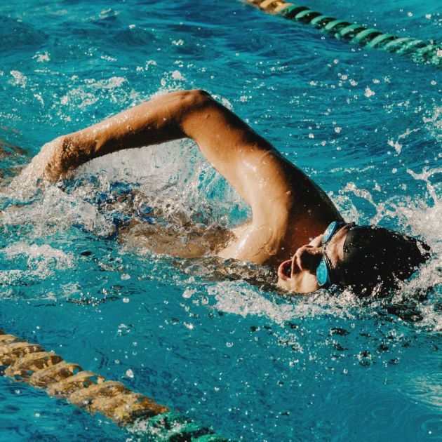 A man swimming in the water with swimming cap and goggles.