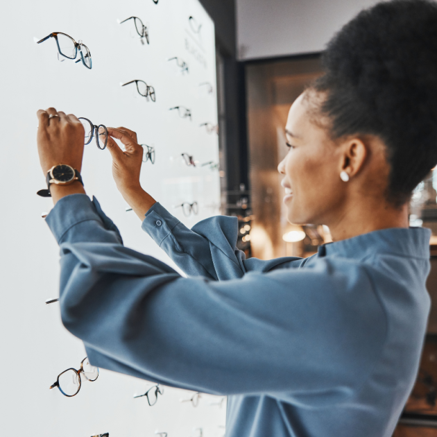 A woman selecting a frame for her prescription lenses at an optical store, surrounded by a variety of stylish eyewear options.