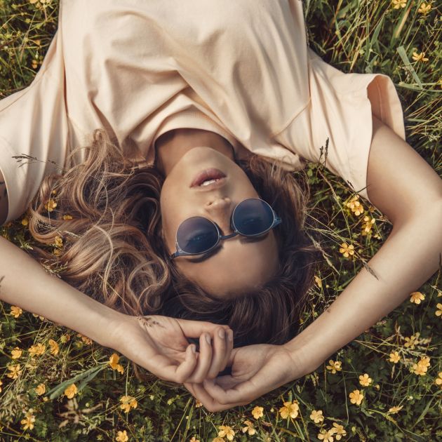 A woman lying down on grass with flowers, wearing MODO ECO eyewear.